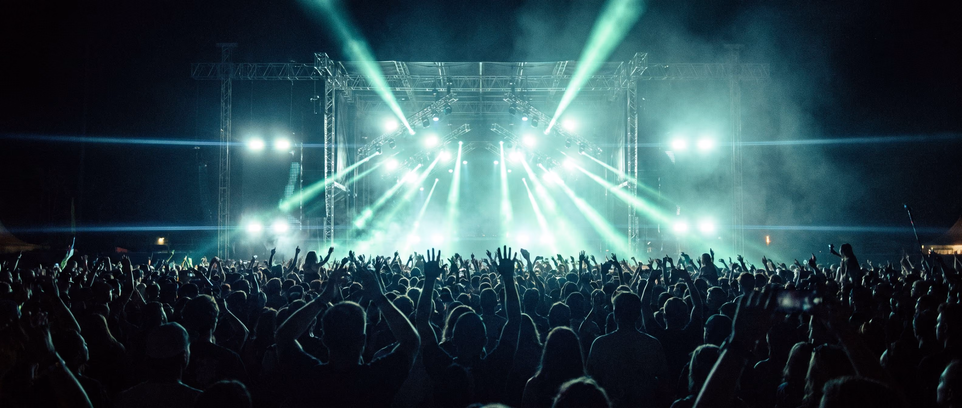 Concert crowd silhouetted against green and cyan stage lighting
