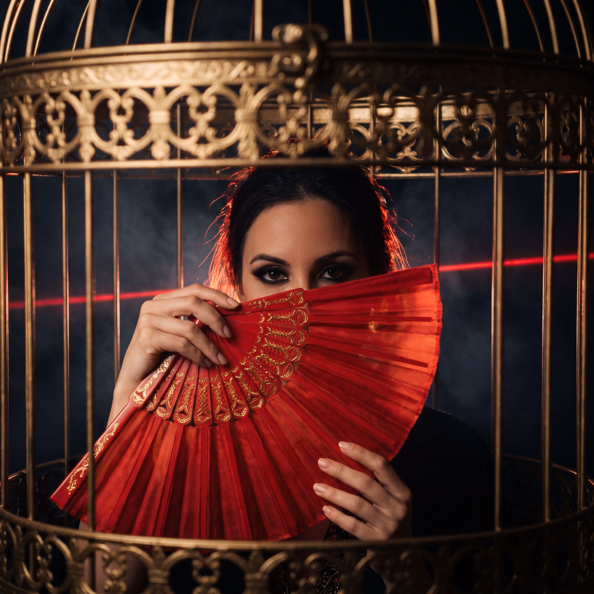 A dancer's eyes above an open red silk fan inside a gold cage