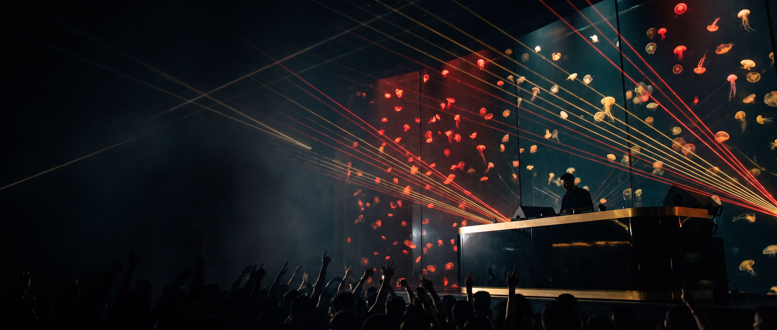 The DJ booth in The Deep, lit red in front of the glowing Jellyfish Wall, laser beams fanning over a crowd