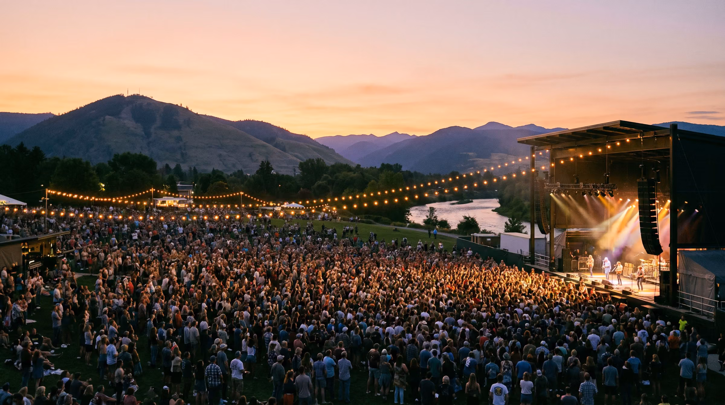 The lawn at Garden City Amphitheater at dusk with the stage lit and the mountains behind