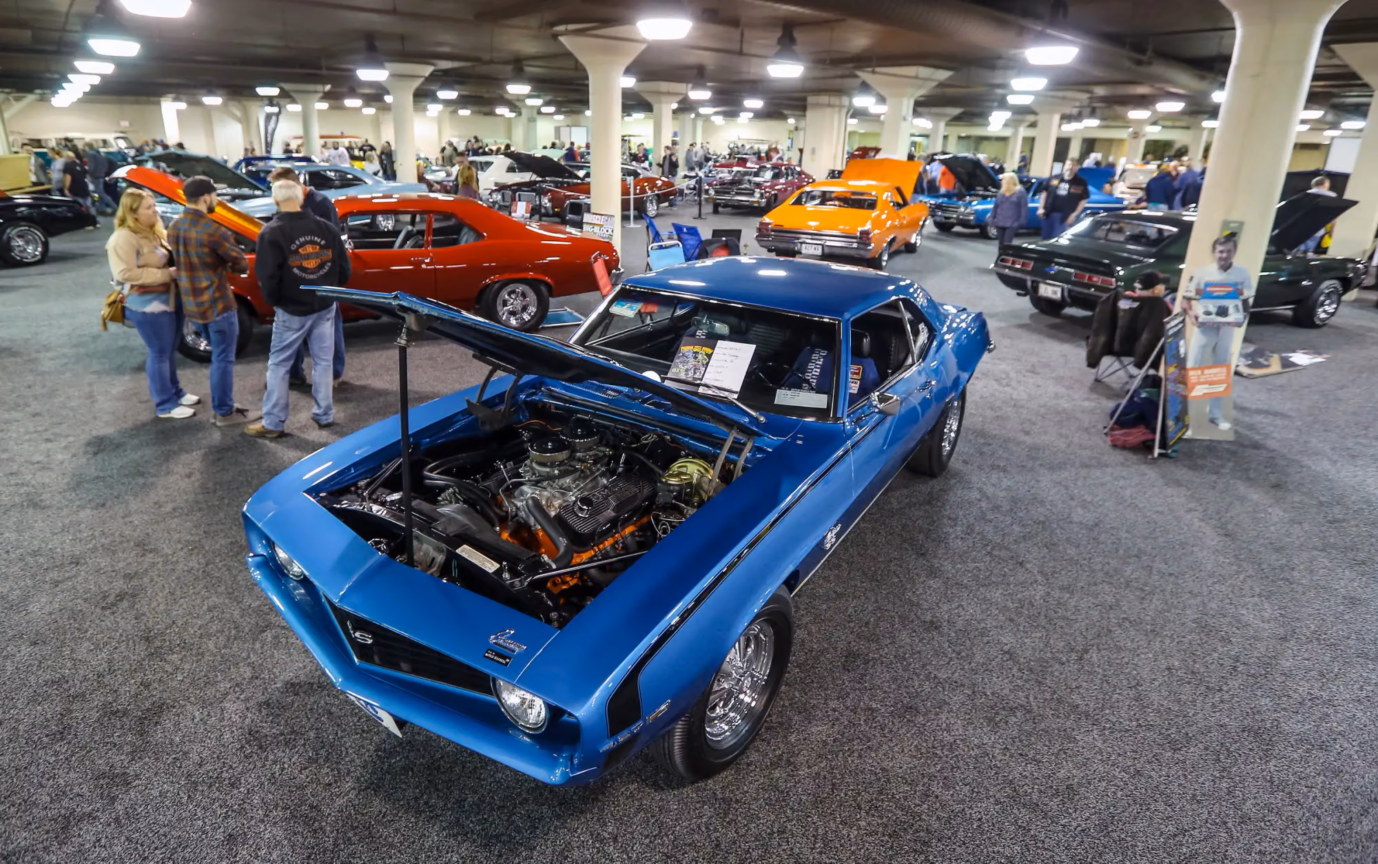 A blue Camaro with its hood up in a row of show cars