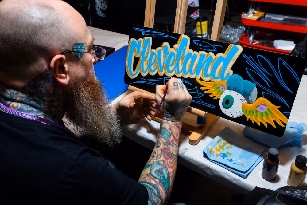 A pinstriper lettering Cleveland on a panel