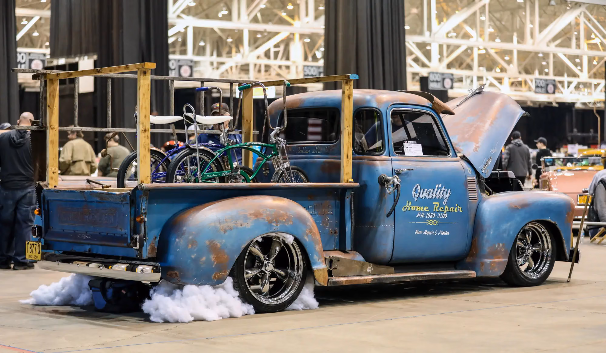 A blue patina pickup with smoke rolling out from under it