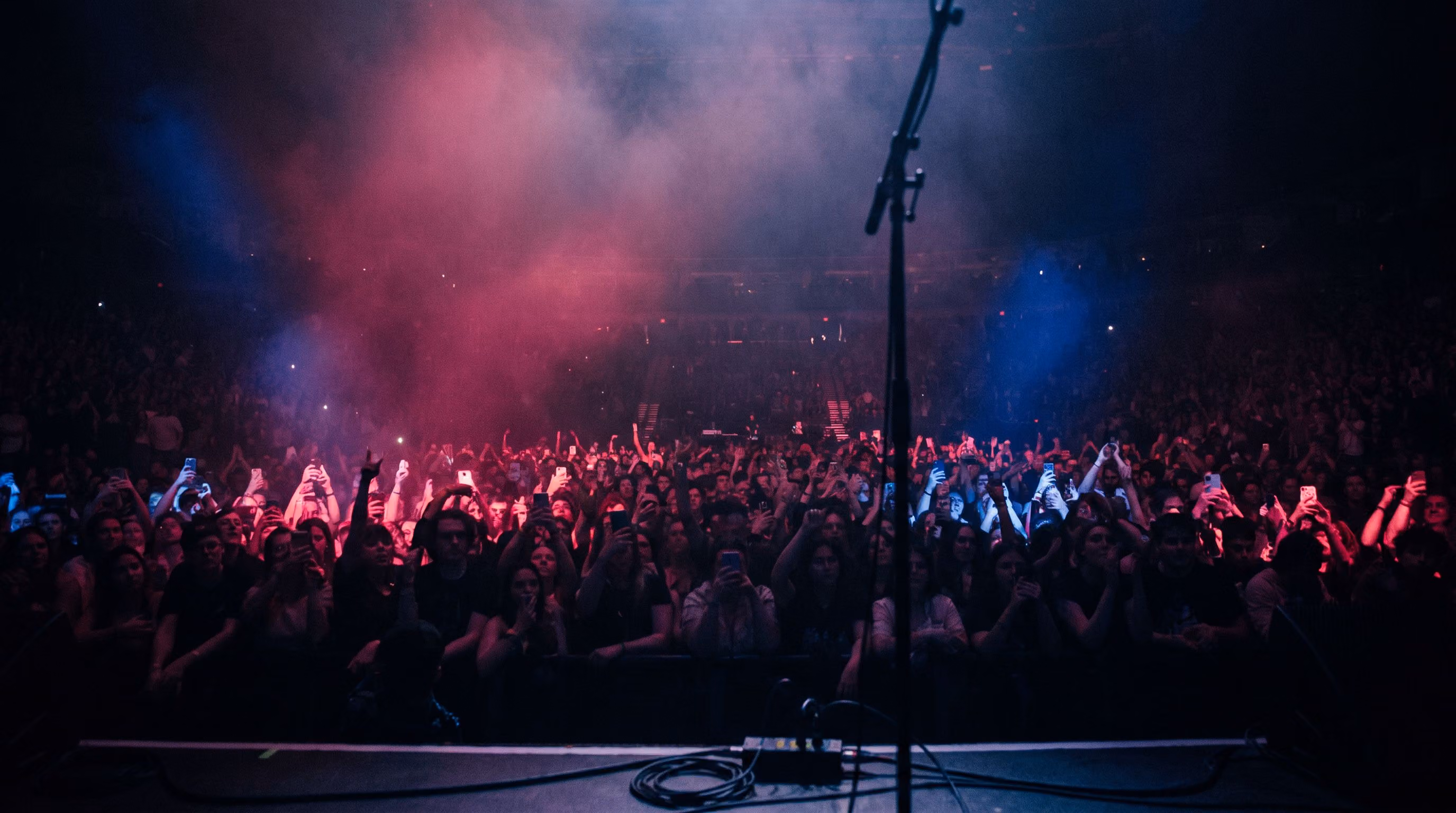 View from the stage of a packed venue crowd under pink and blue lighting