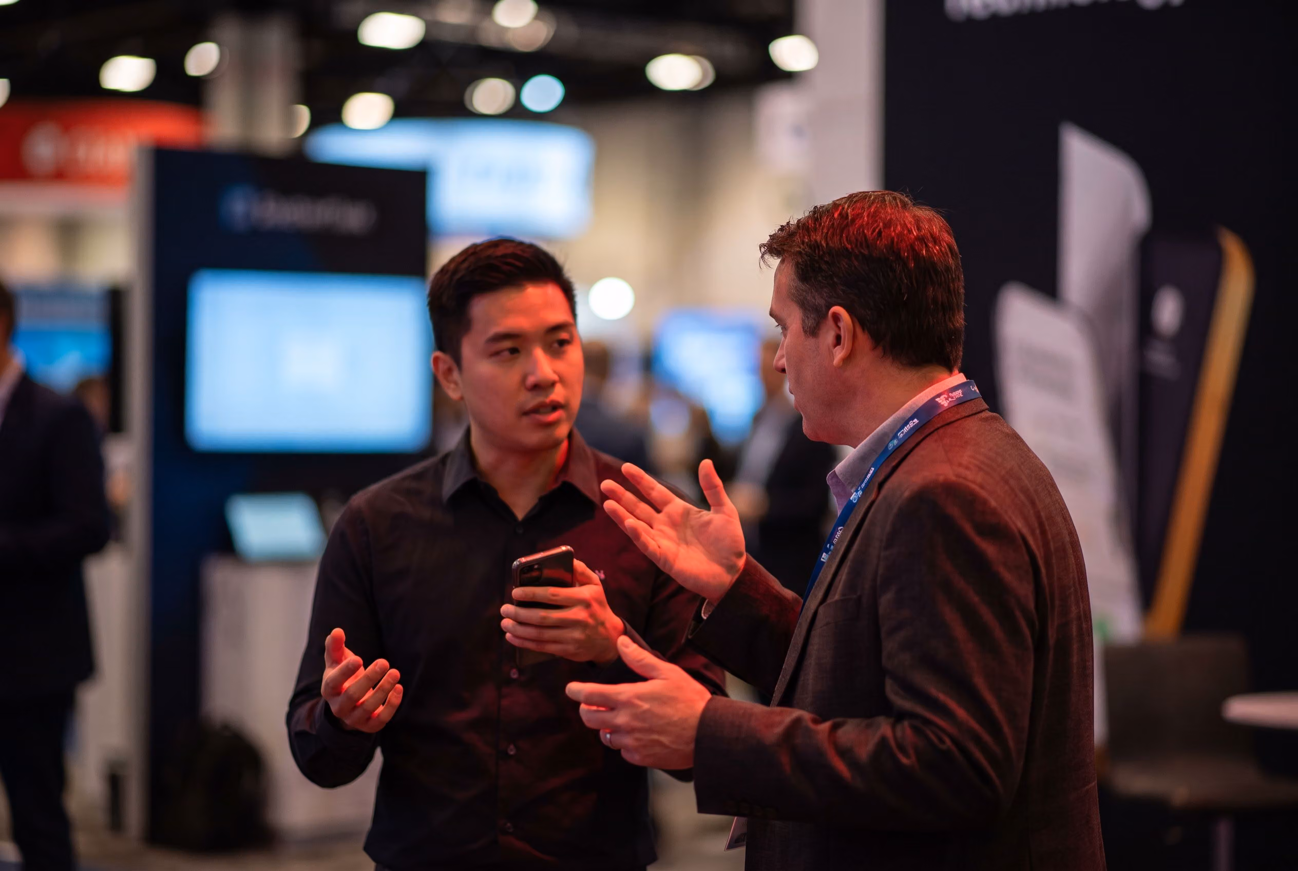 Exhibitor holding a phone while talking with a visitor at a trade show booth