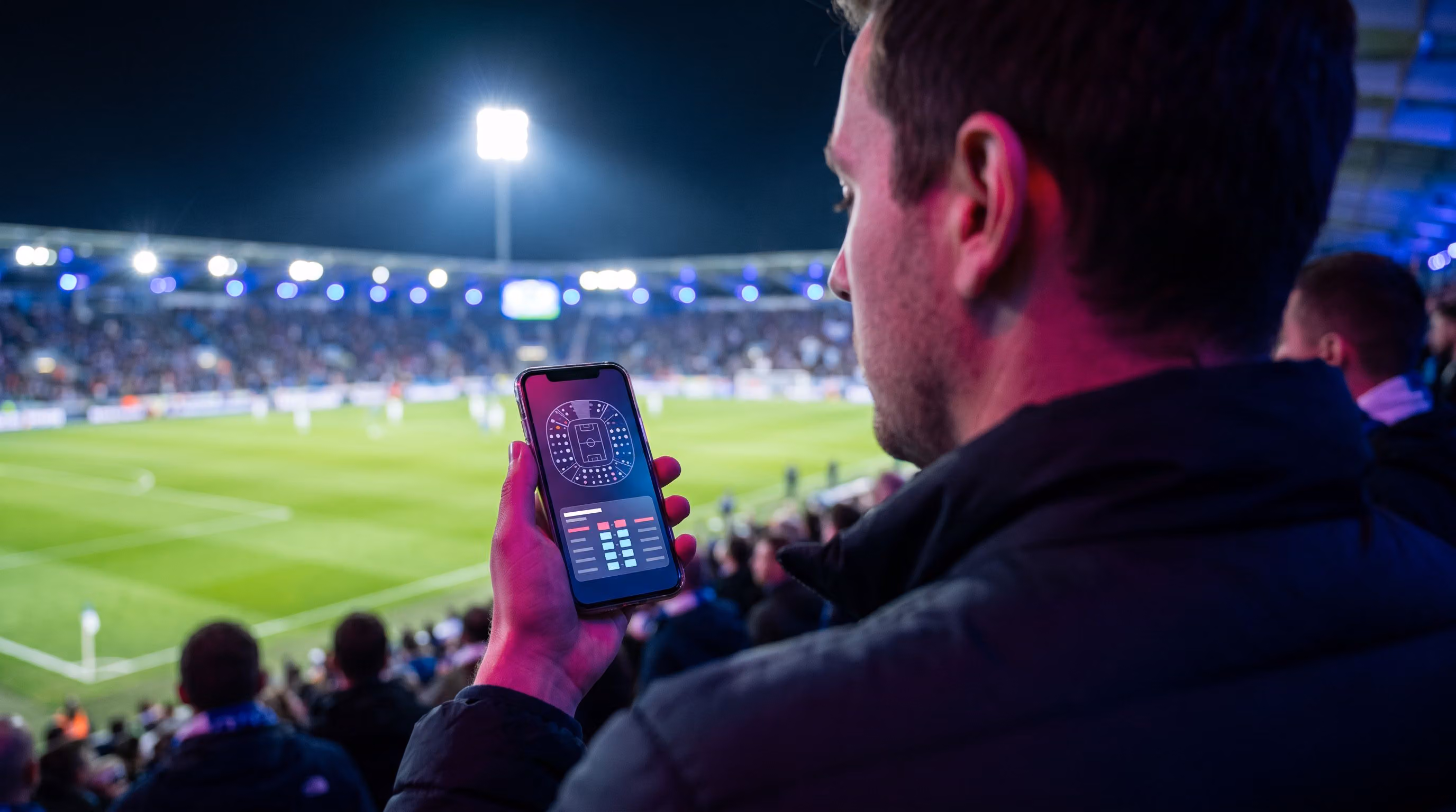 Fan checking a phone in the stadium stands during a night game