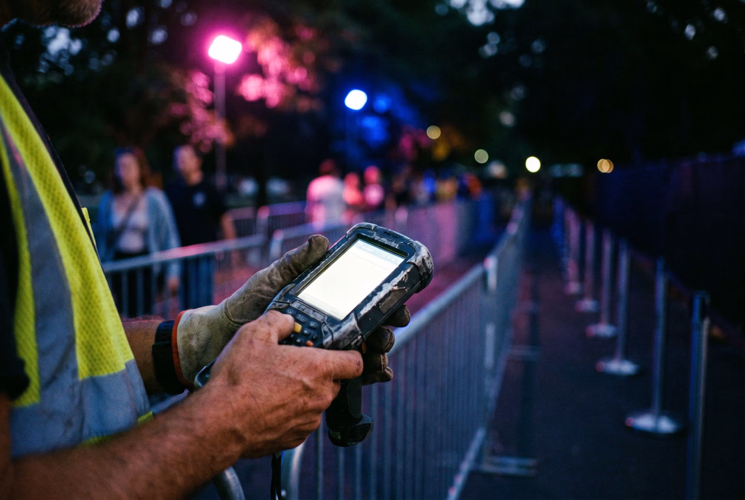 Hands holding a ticket scanner at an event entry gate at dusk