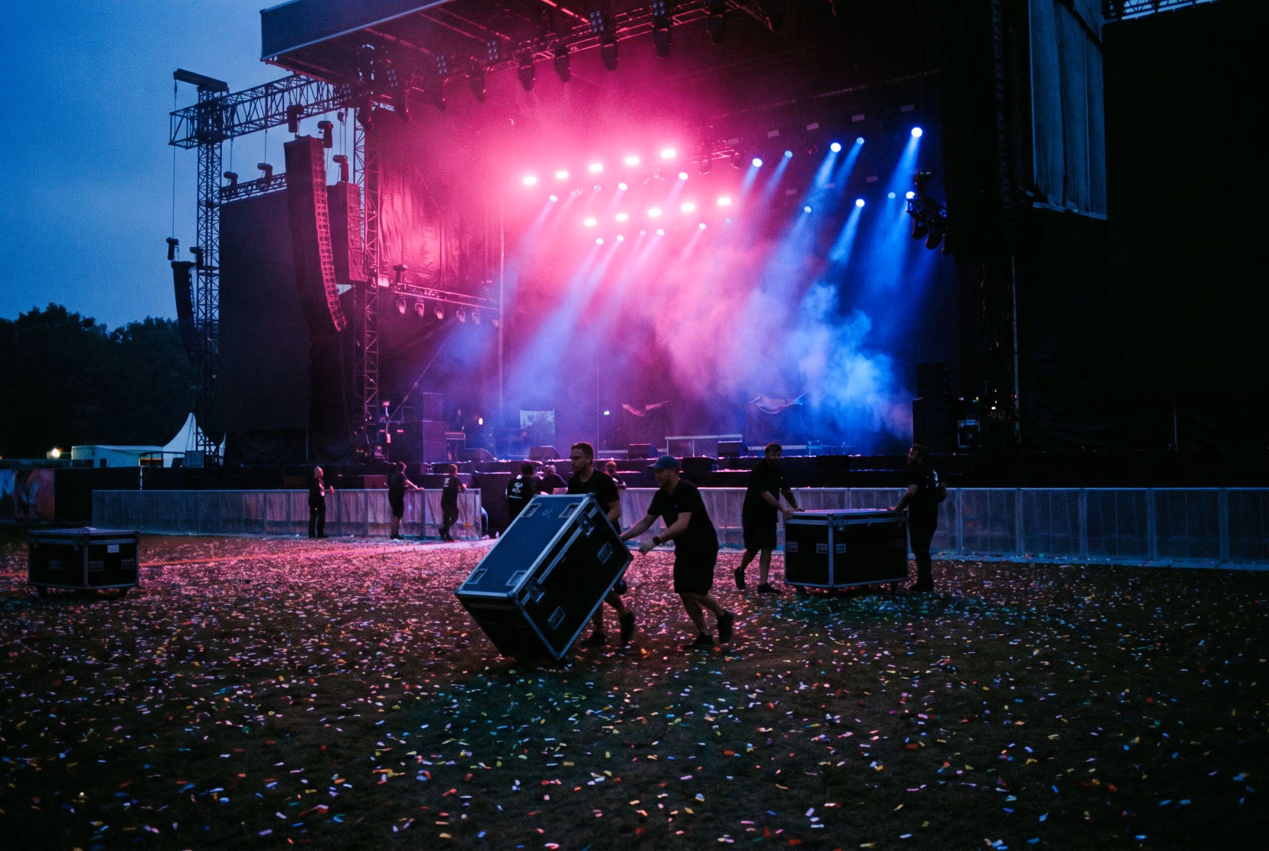Crew rolling road cases across festival grounds after the show at blue hour
