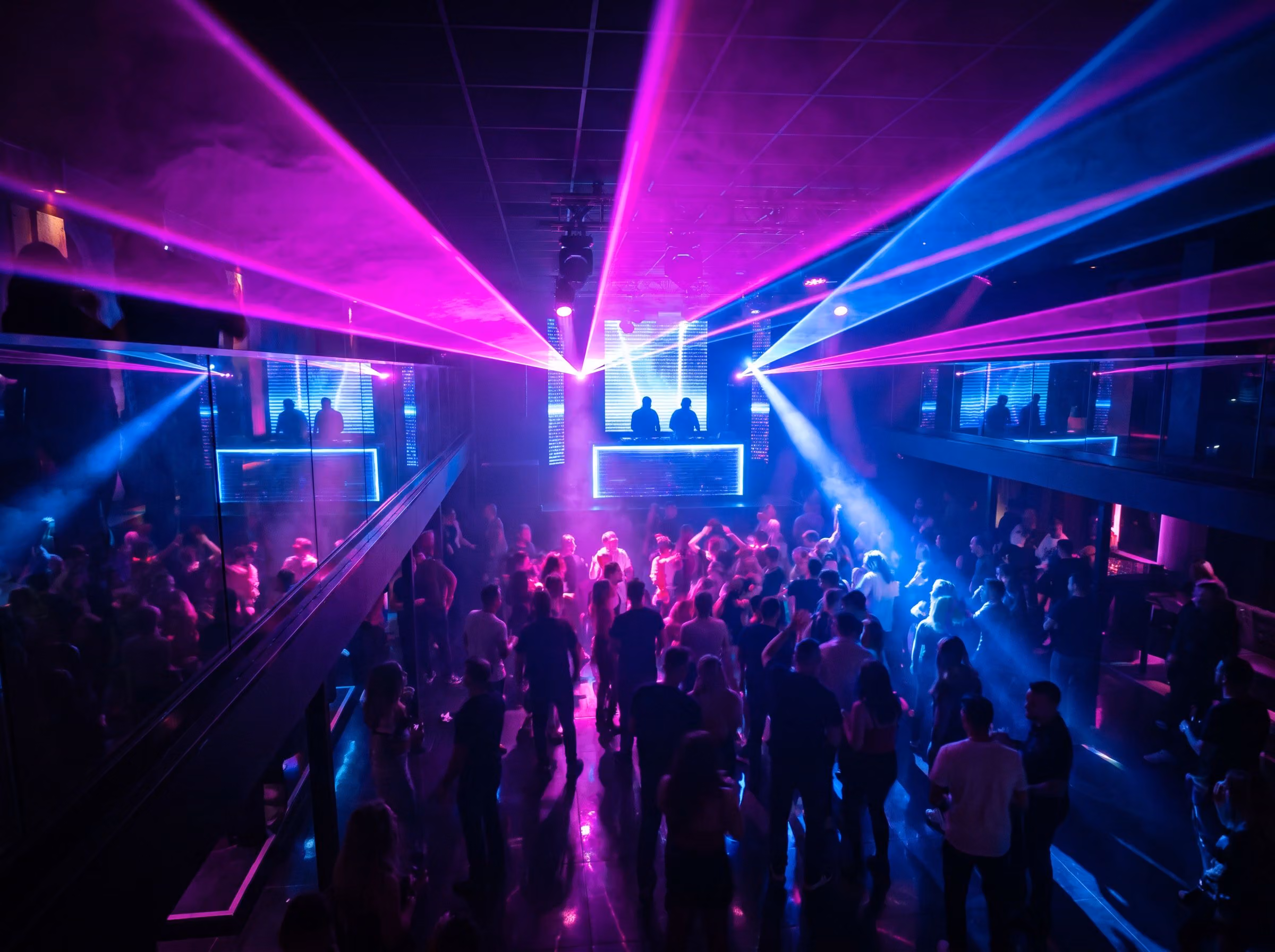 Packed nightclub dance floor under pink and blue lasers
