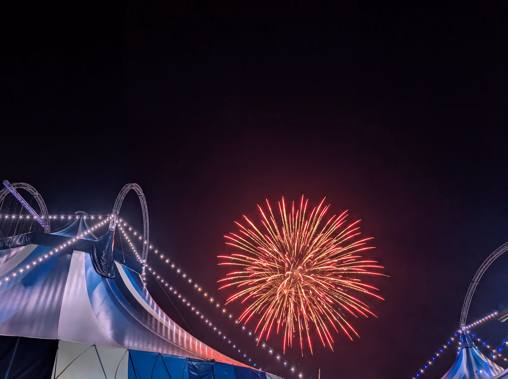 Aerial night view of the Wonderland big top glowing on the event grounds