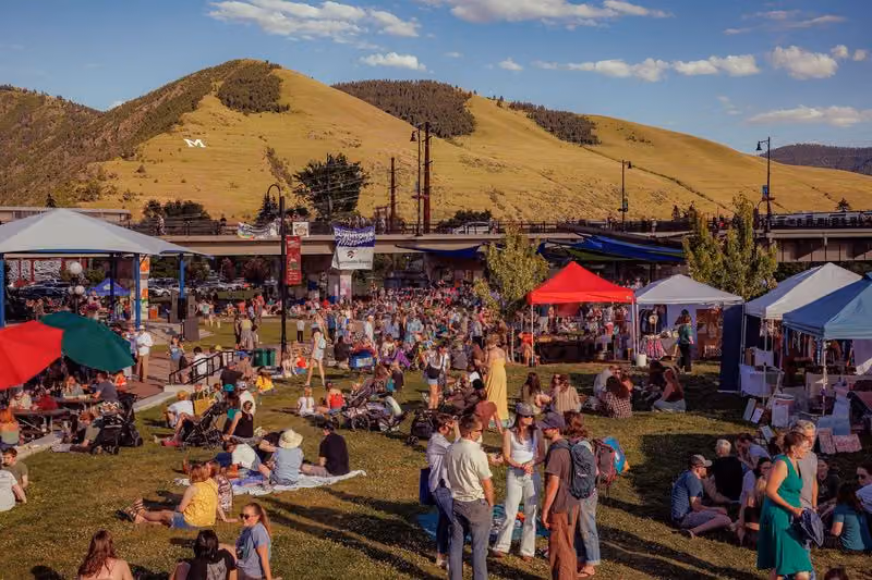 Vendor tents and festival crowd below a grassy mountain