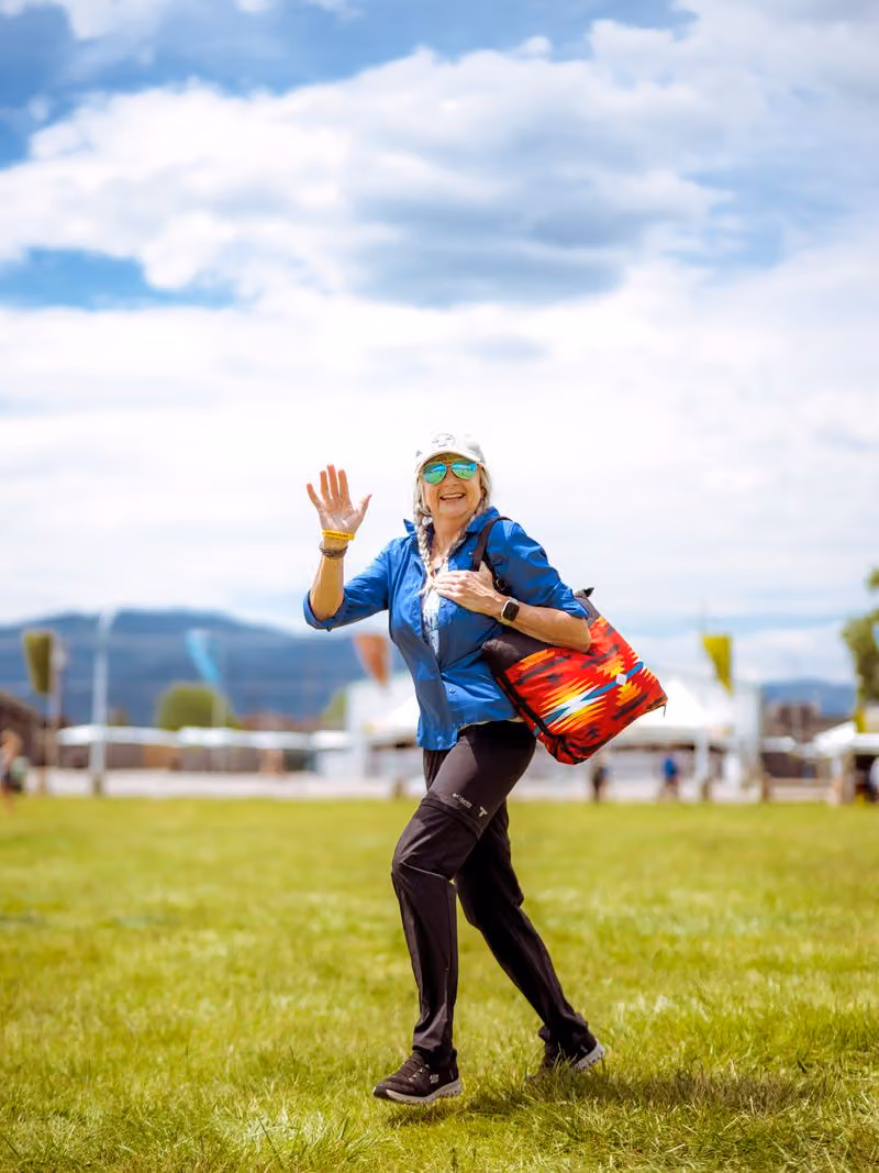 Festivalgoer waving on the lawn with mountains behind